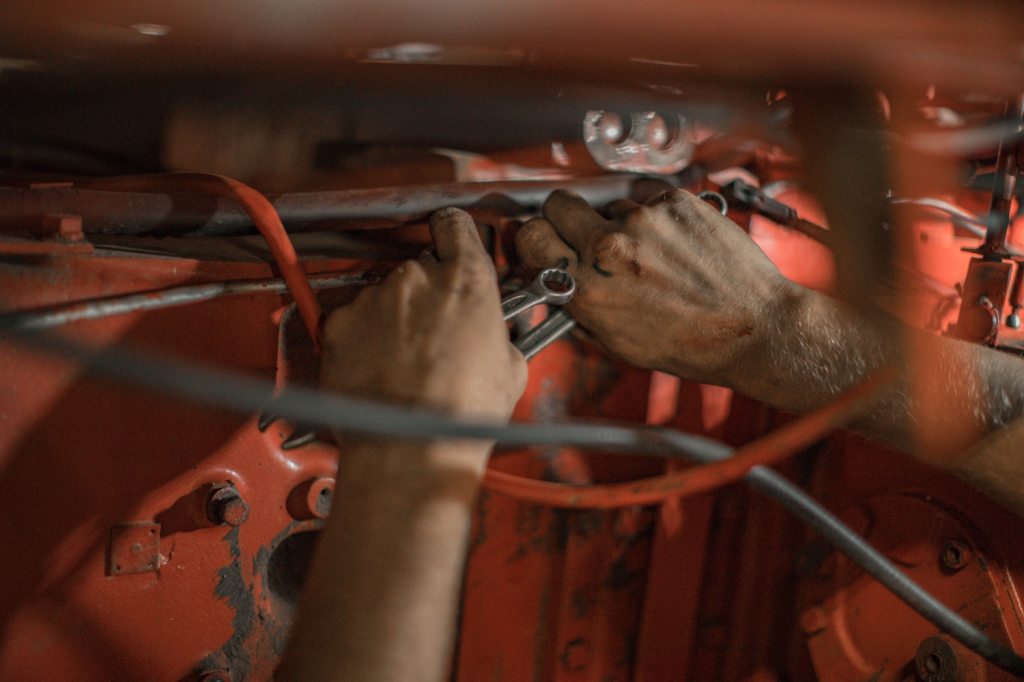 A mechanic's hands spinning a wrench, an engine bay's firewall visible behind.