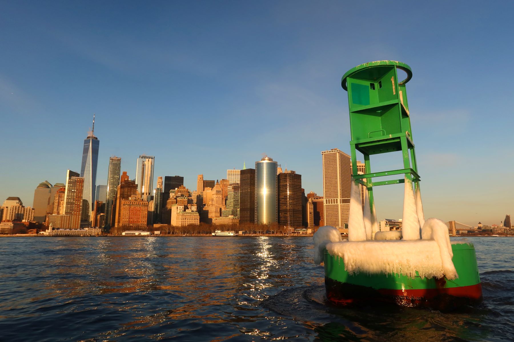 A green buoy covered in ice in the New York Harbor area of lower Manhattan and the One World Trade Center