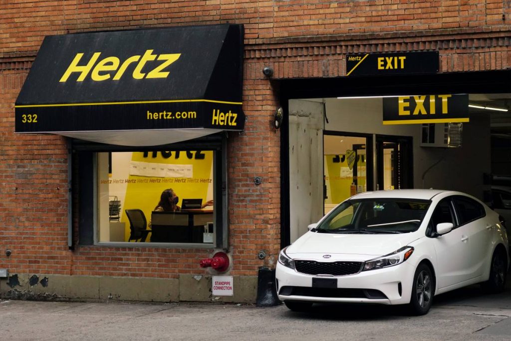 A white rental car pulls out of a Hertz rental car company location in New York City