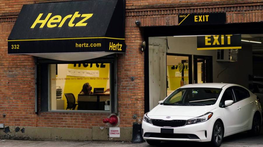 A white rental car drives out of a Hertz rental car company location in New York City