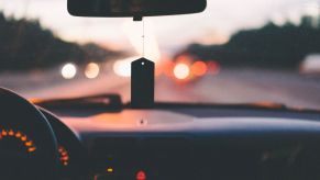 Artistic, blurred shot of the dashboard of a car. You can see headlights and taillights out of the windshield, and there's a tag hanging from the rearview mirror