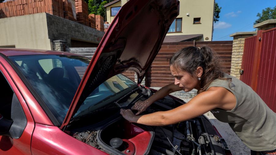 A woman inspecting and performing maintenance on her car engine under the hood of her vehicle in Kiev, Ukraine