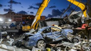 A yellow excavator pulls apart a busted old blue car at a junkyard