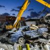 A yellow excavator pulls apart a busted old blue car at a junkyard