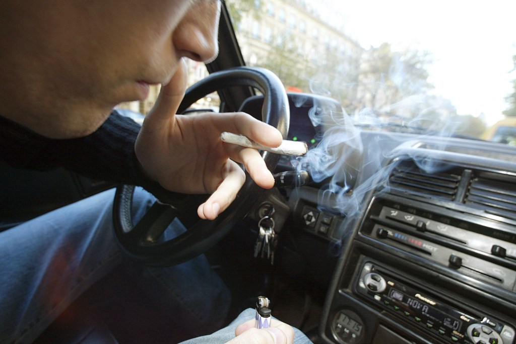 A man smokes a hand-rolled cigarette inside his car.