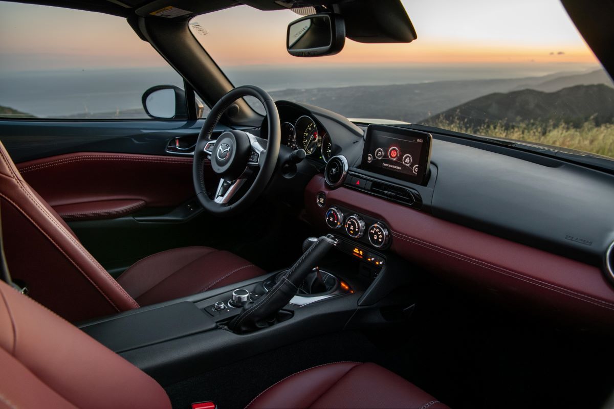 Mazda Miata interior, showing the infotainment system, telescoping wheel, shifter, and moveable cupholders