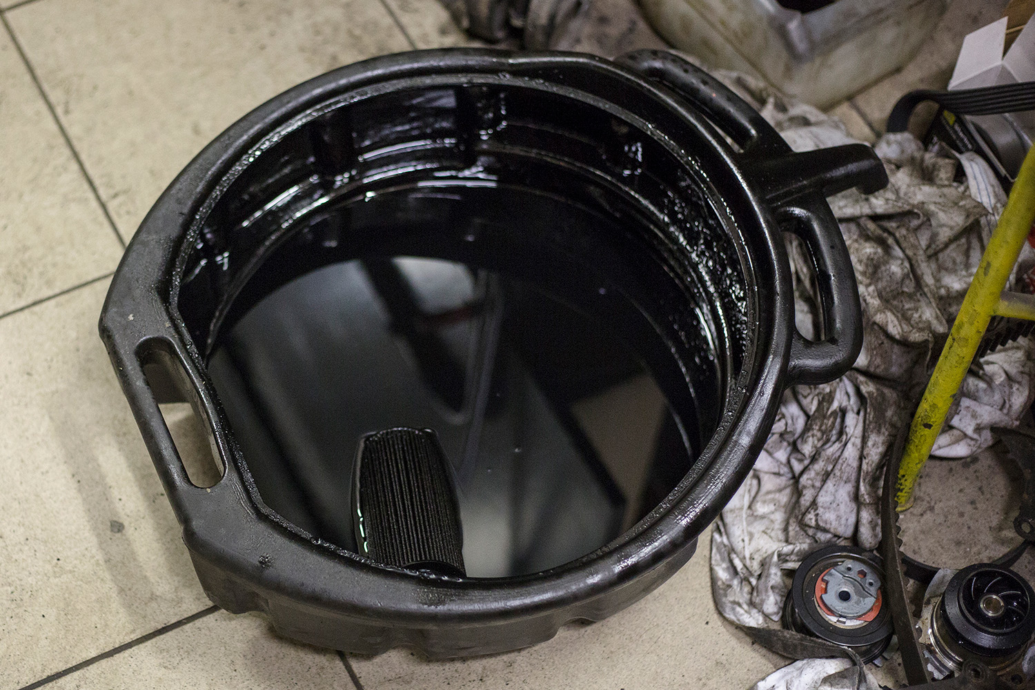 Open top oil drain pan with spout full of used engine oil after change