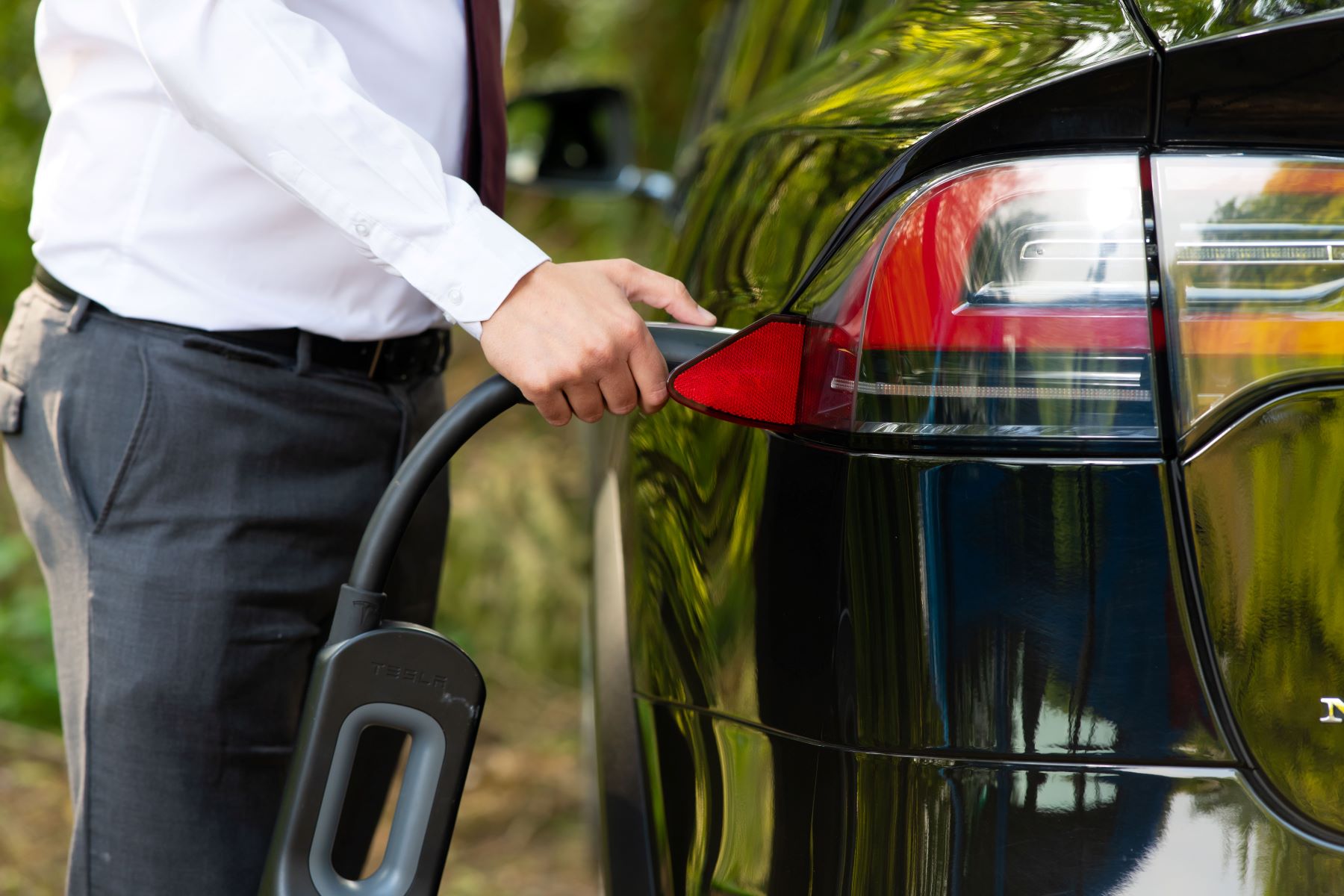 A man plugging-in the charging cable to his Tesla Model X electric vehicle (EV)