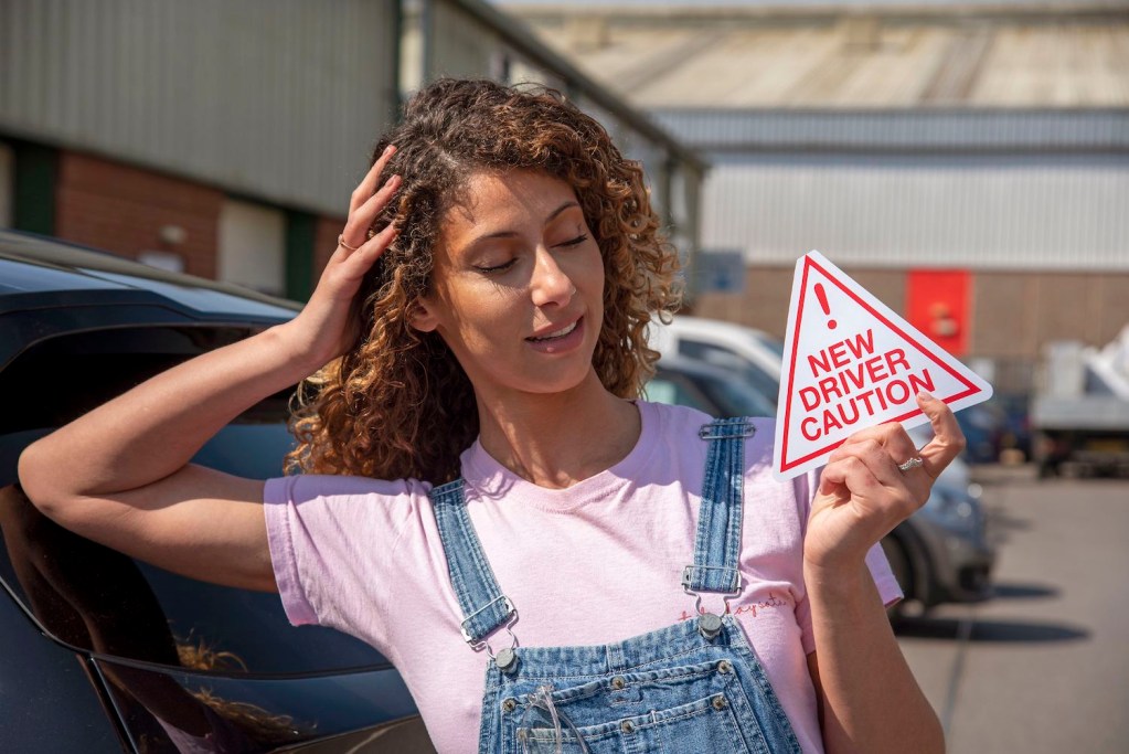 A new driver holding a new driver caution sign to display on her car after passing the driving test