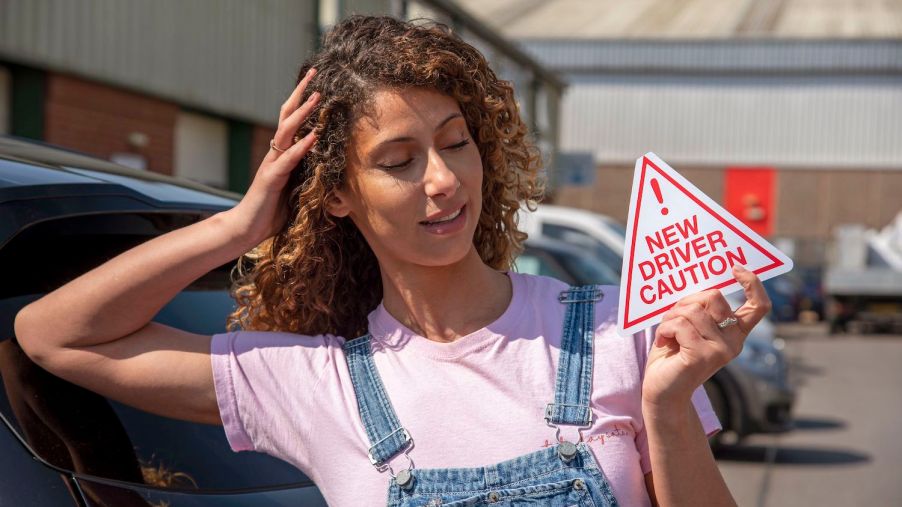 A new driver holding a new driver caution sign to display on her car after passing the driving test