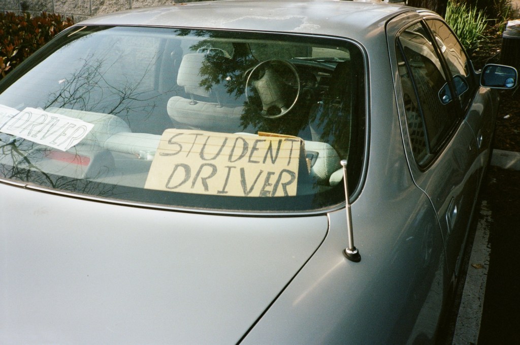 student driver back view of car with handwritten sign reading