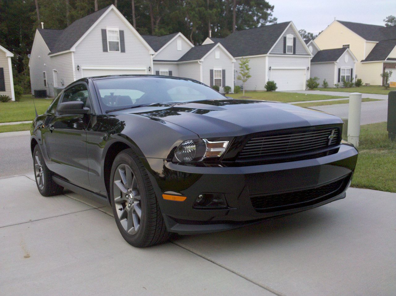 Black 2011 Ford Mustang fastback coupe parked in the driveway of a suburban neighborhood