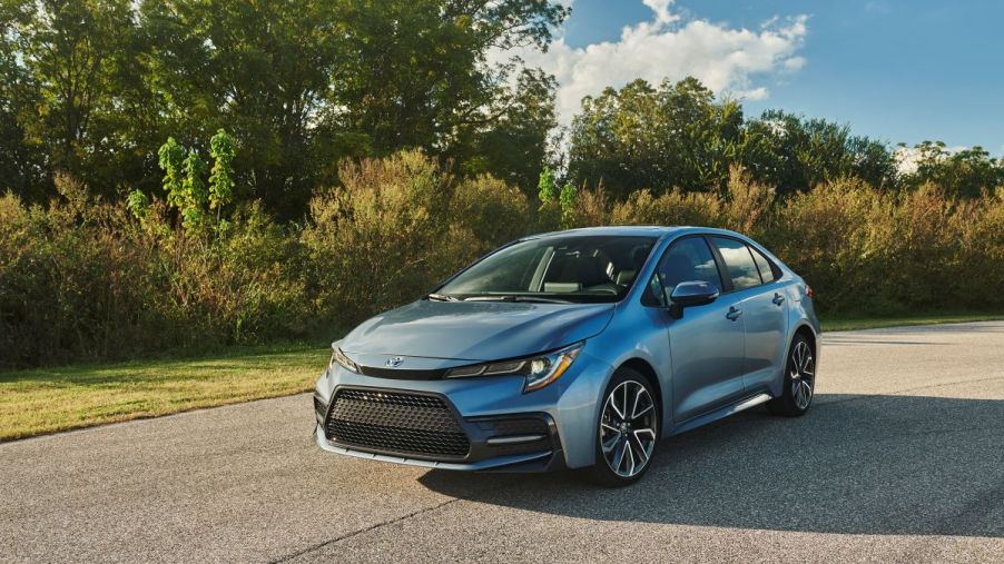 Used 2020 Toyota Corolla sedan in grey, parked on pavement in front of trees and bushes on a summer day
