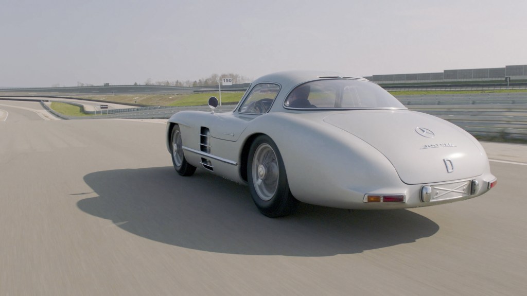 The rear 3/4 view of the silver 1955 Mercedes-Benz 300 SLR Uhlenhaut Coupe driving on a racetrack