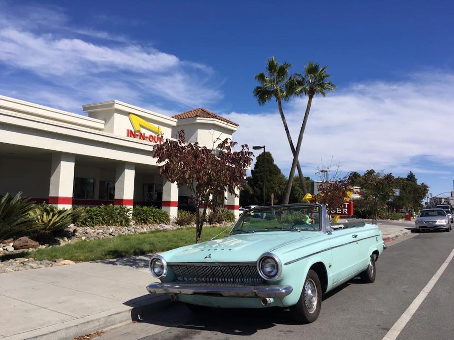 Blue convertible parked in front of palm trees and an In-N-Out burger.