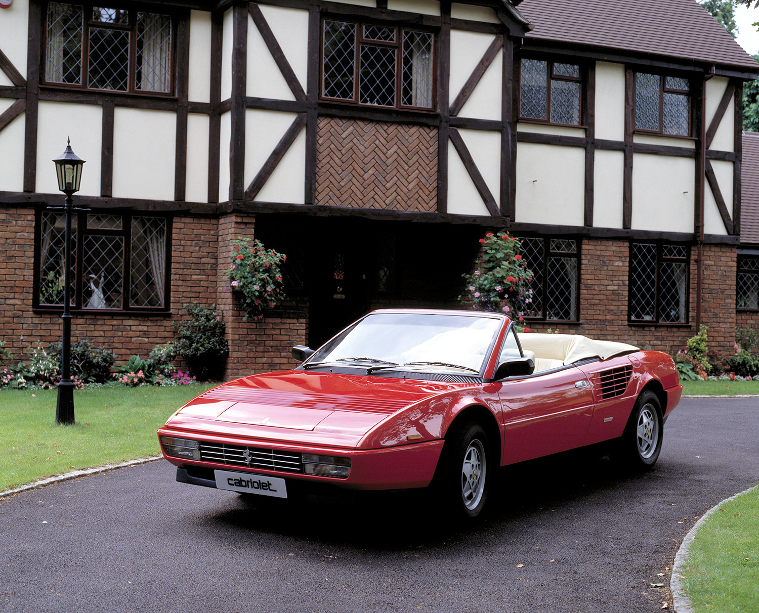 Red Ferrari Mondial Cabriolet parked in front of a house, this is the cheapest Ferrari one can currently buy