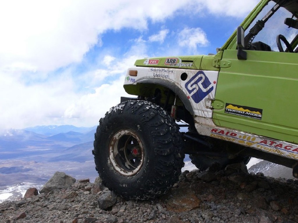 Closeup of a 1986 Suzuki Samurai's wheel parked atop a mountain, a valley visible below.