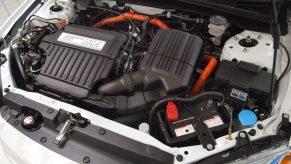The engine bay of a silver 2003 Honda Civic Hybrid showing its 12-volt lead-acid car battery