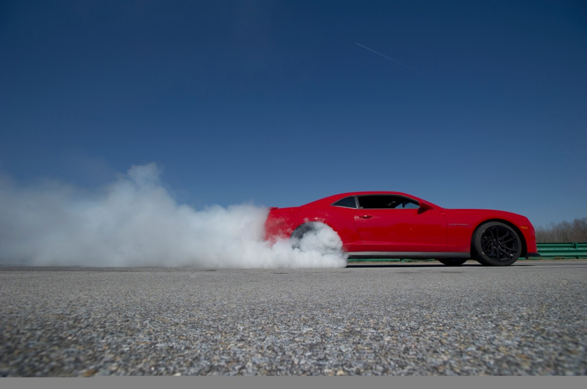 Red 2013 Chevrolet Camaro ZL1 doing a burnout on tarmac for Chevry press photo shoot