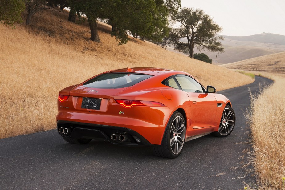 The rear 3/4 view of an orange 2015 Jaguar F-Type R Coupe on a winding plains road