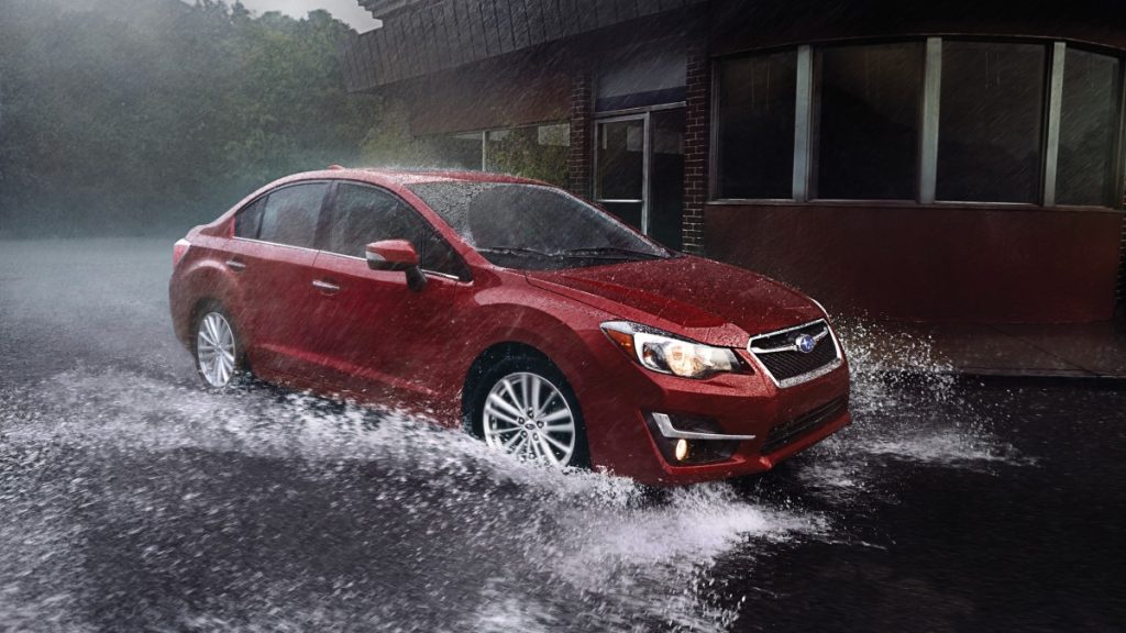 a 2016 red subaru impreza tackles a big puddle with ease thanks to standard four-wheel drive, a unique feature for compact cars