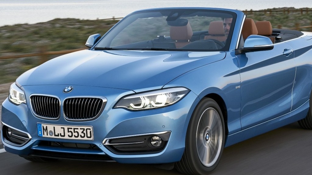 a light blue 2018 bmw 2 series, an exciting convertible driving along a road with an ocean behind it