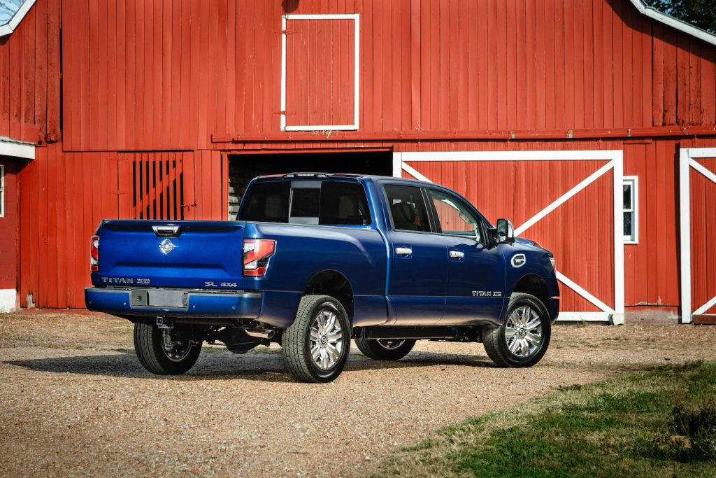 Blue Nissan Titan XD pickup truck parked in front of a red barn.