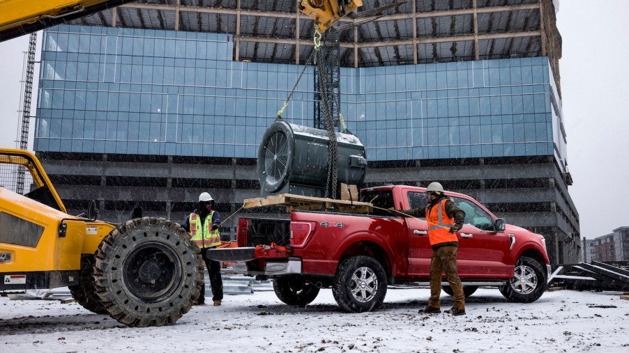Construction workers setting a heavy piece of equipment in the bed of a half-ton Ford pickup truck.