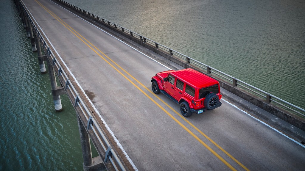 Hardtop Jeep Wrangler 4xe SUV driving away from the camera, across a bridge.