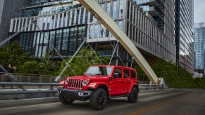 A red Jeep Wrangler 4xe plug-in hybrid driving through a city.