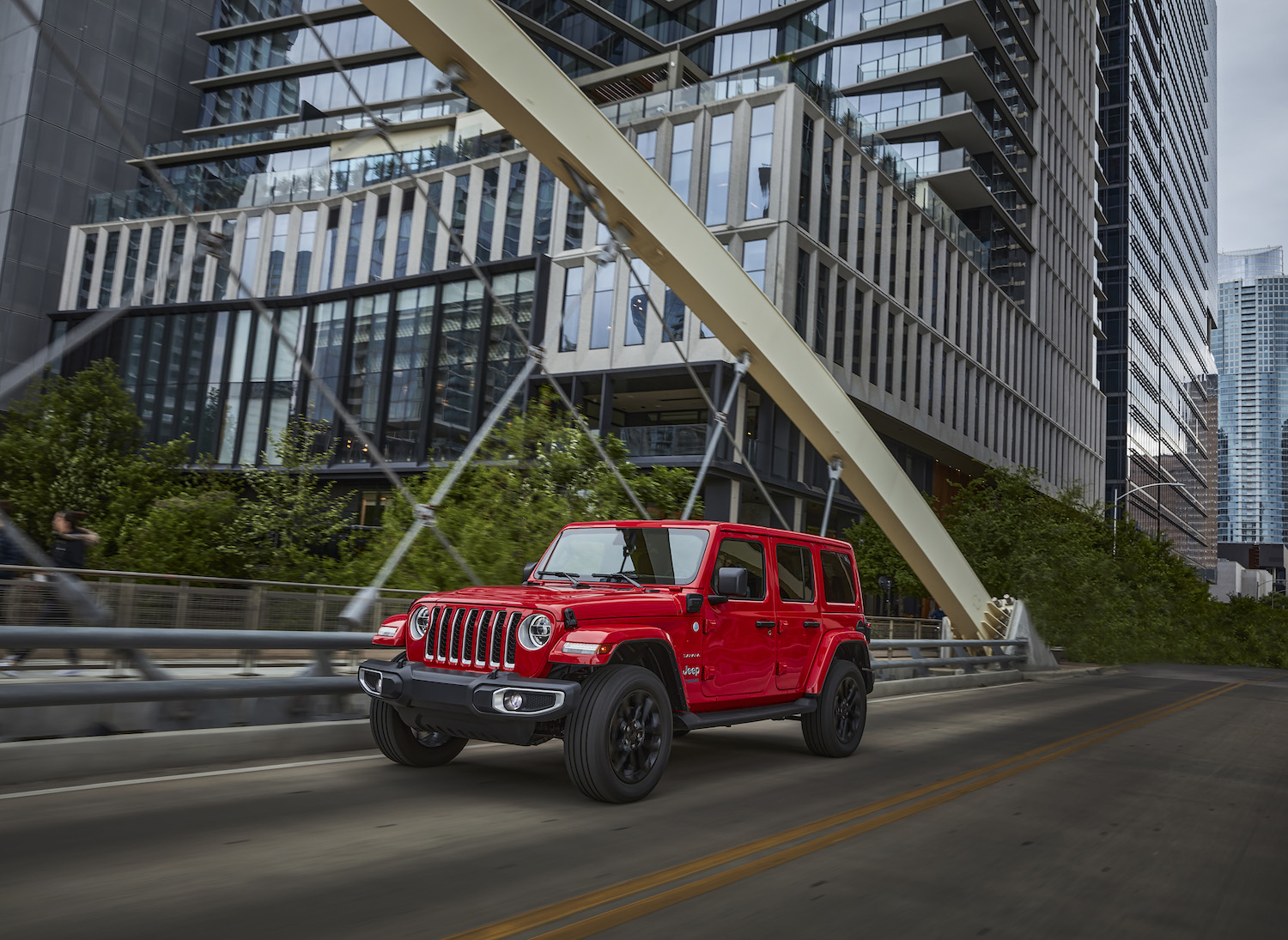 A red Jeep Wrangler 4xe plug-in hybrid driving through a city.