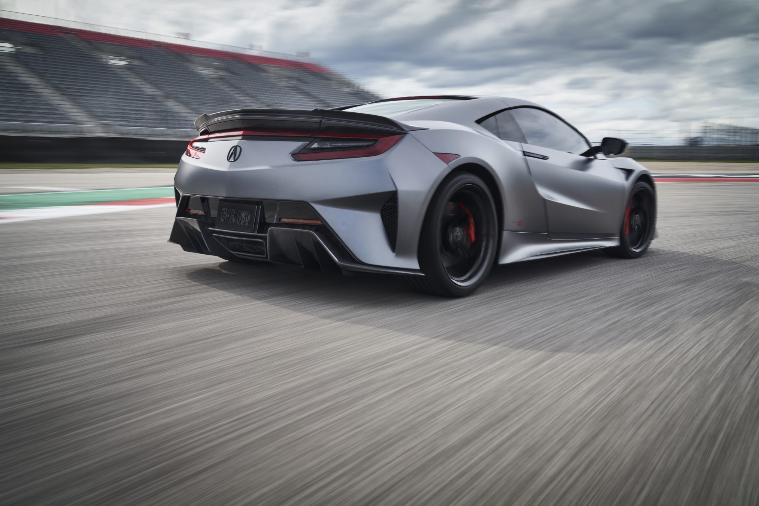 The rear 3/4 view of a matte-gray 2022 Acura NSX Type S going around a racetrack corner at speed