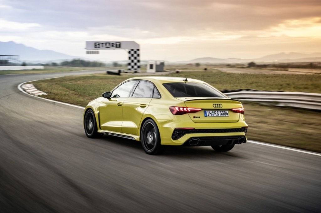 The rear 3/4 view of a yellow 2022 Audi RS3 driving around a racetrack