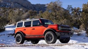A red 2022 Ford Bronco Wildtrak model with option HOSS 3.0 parked on a snowy off-road trail in a forest