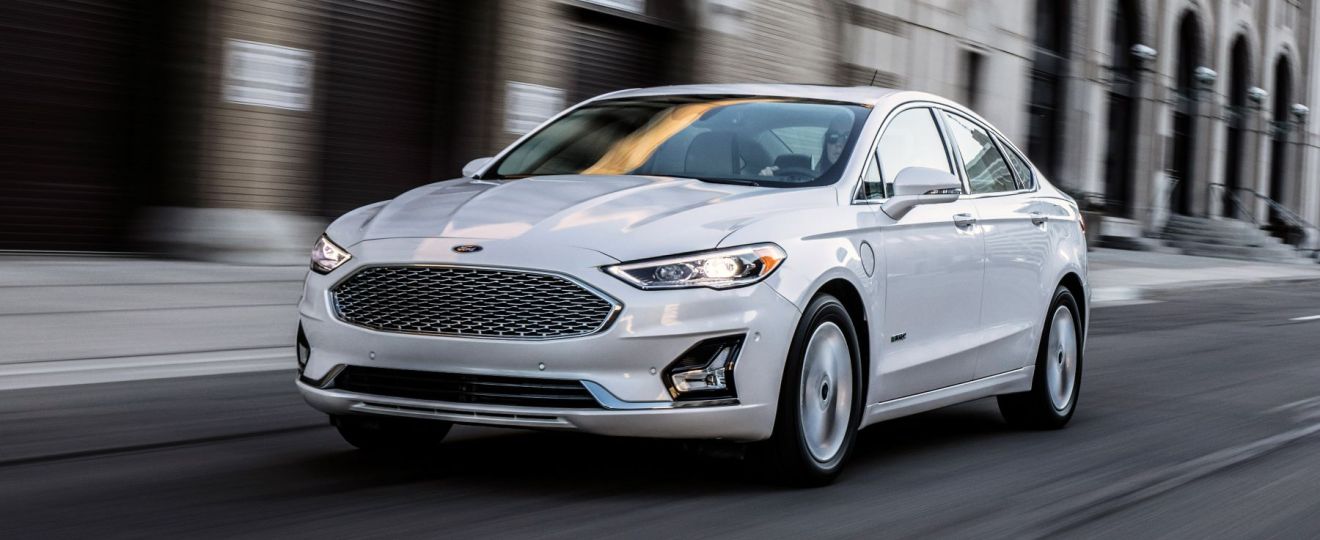 A white 2022 Ford Fusion midsize sedan model driving through a metropolitan city