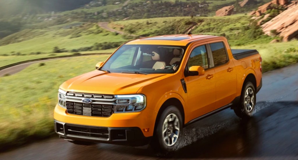 A yellow 2022 Ford Maverick small pickup truck is driving on a wet road. 
