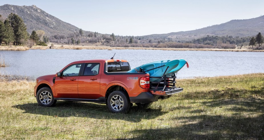 An orange 2022 Ford Maverick Lariat compact pickup truck model parked near a forest lake with a canoe in its truck bed