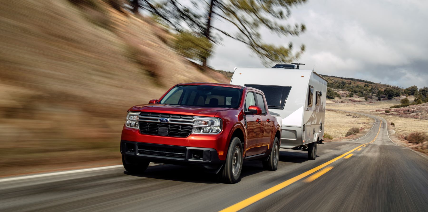 A red 2022 Ford Maverick Lariat towing an RV camper motorhome down a stretch of country highway