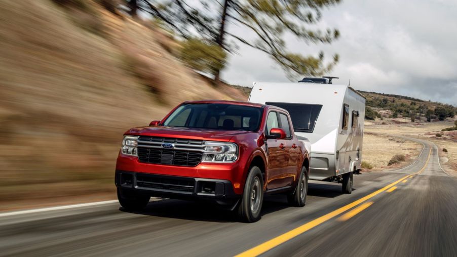 A red 2022 Ford Maverick Lariat towing an RV camper motorhome down a stretch of country highway