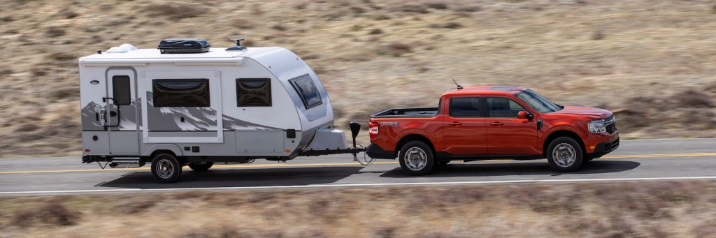 Red Ford Maverick compact pickup truck towing a trailer.
