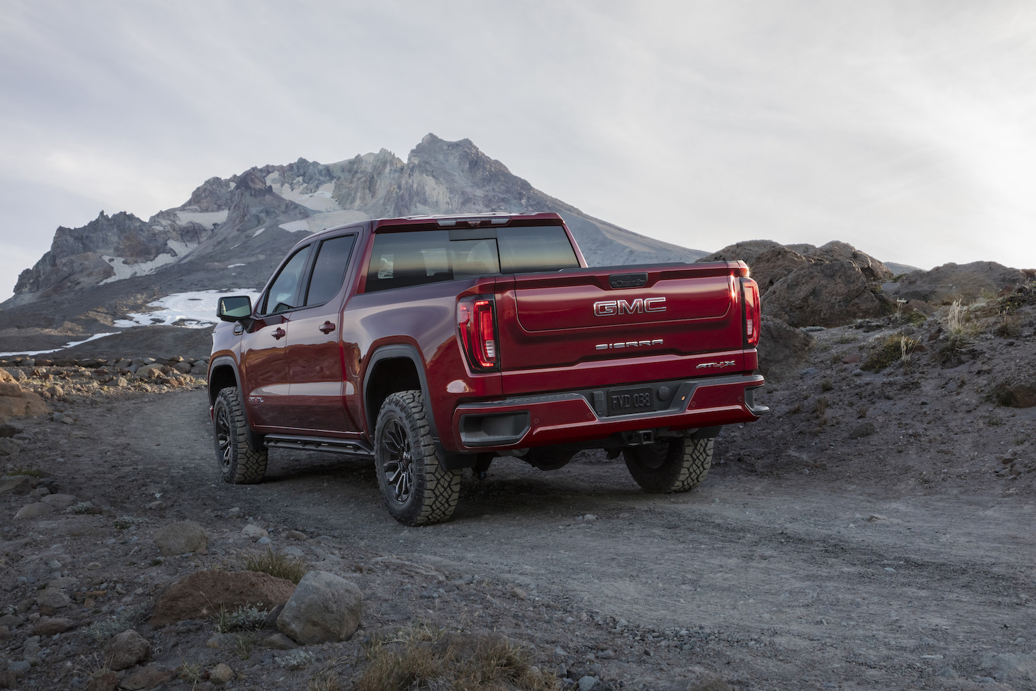 Red GMC Sierra half-ton pickup truck driving along a dirt trail through snowy mountains.