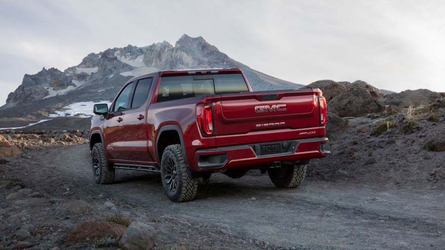 Red GMC Sierra half-ton pickup truck driving along a dirt trail through snowy mountains.