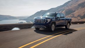A blue 2022 GMC Sierra on a road in front of a mountain and a body of water.