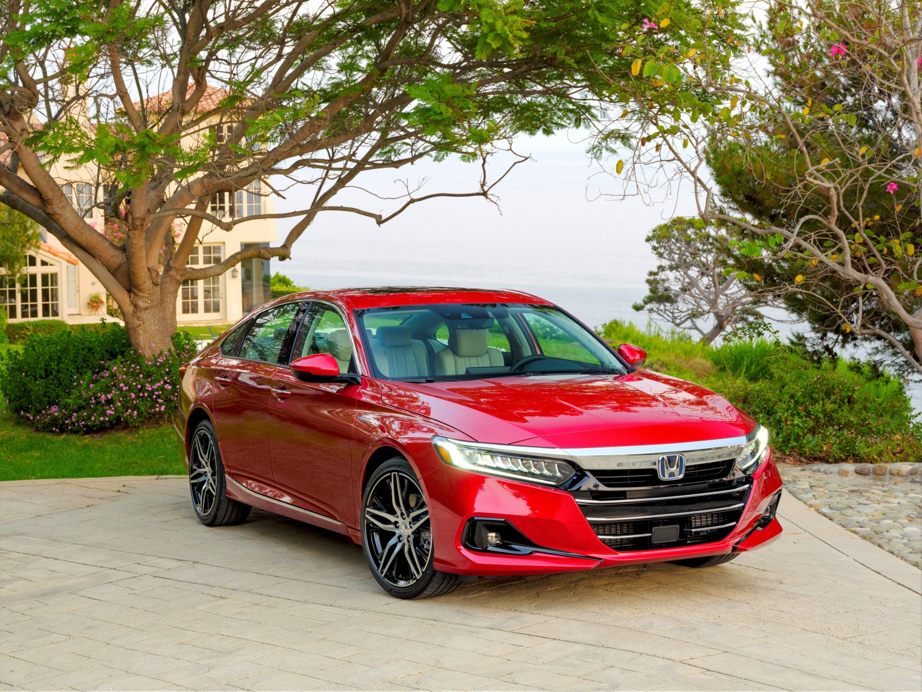 A red 2022 Honda Accord Hybrid midsize sedan parked on a stone plaza outside of a luxury home