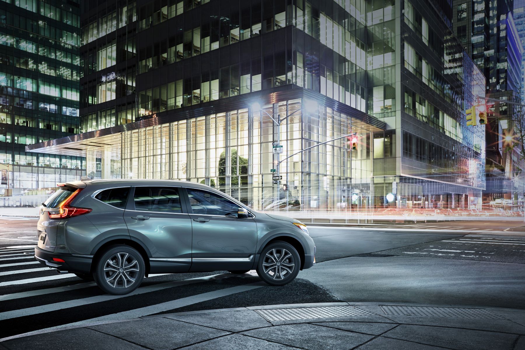 A 2022 Honda CR-V Touring compact SUV model with a gray paint color option driving at a city intersection at night