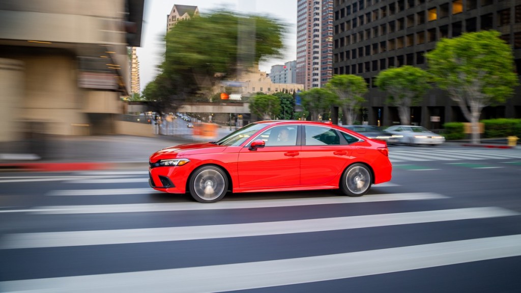 a red 2022 honda civic drives along a city street, showing off its sleek design and comfortable ride