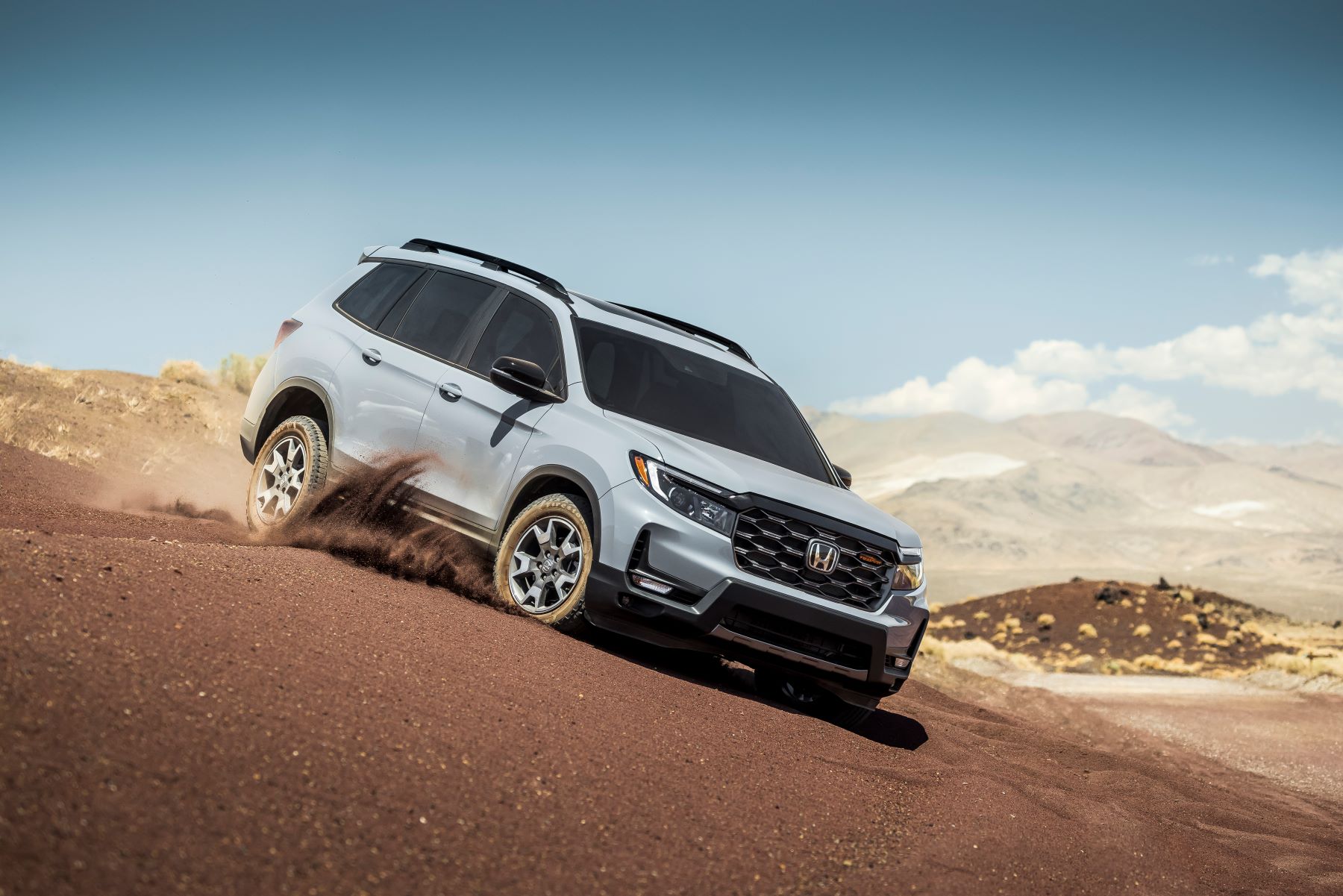 A light gray 2022 Honda Passport TrailSport adventure SUV model driving down a dirt hill, which was graded poorly by the IIHS