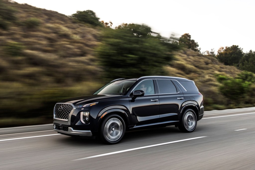 A black 2022 Hyundai Palisade driving down a road in front of a hillside.