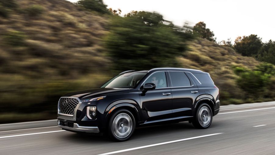 A black 2022 Hyundai Palisade driving down a road in front of a hillside.