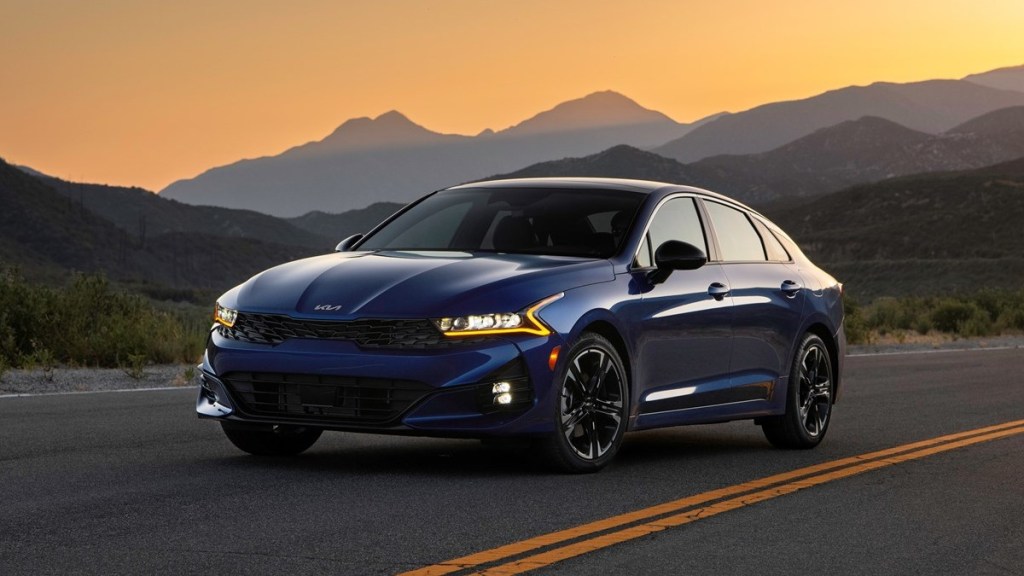 A blue 2022 kia k5 parked at dusk with mountains